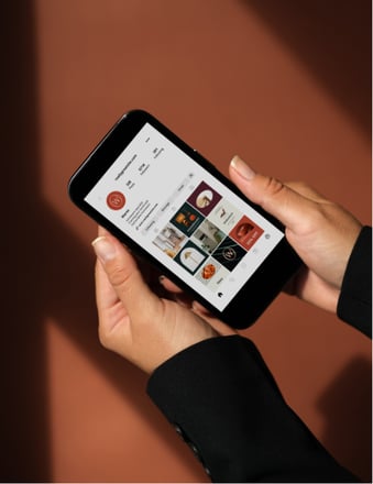 Hands holding a smartphone displaying an Instagram business profile against a warm brown background.